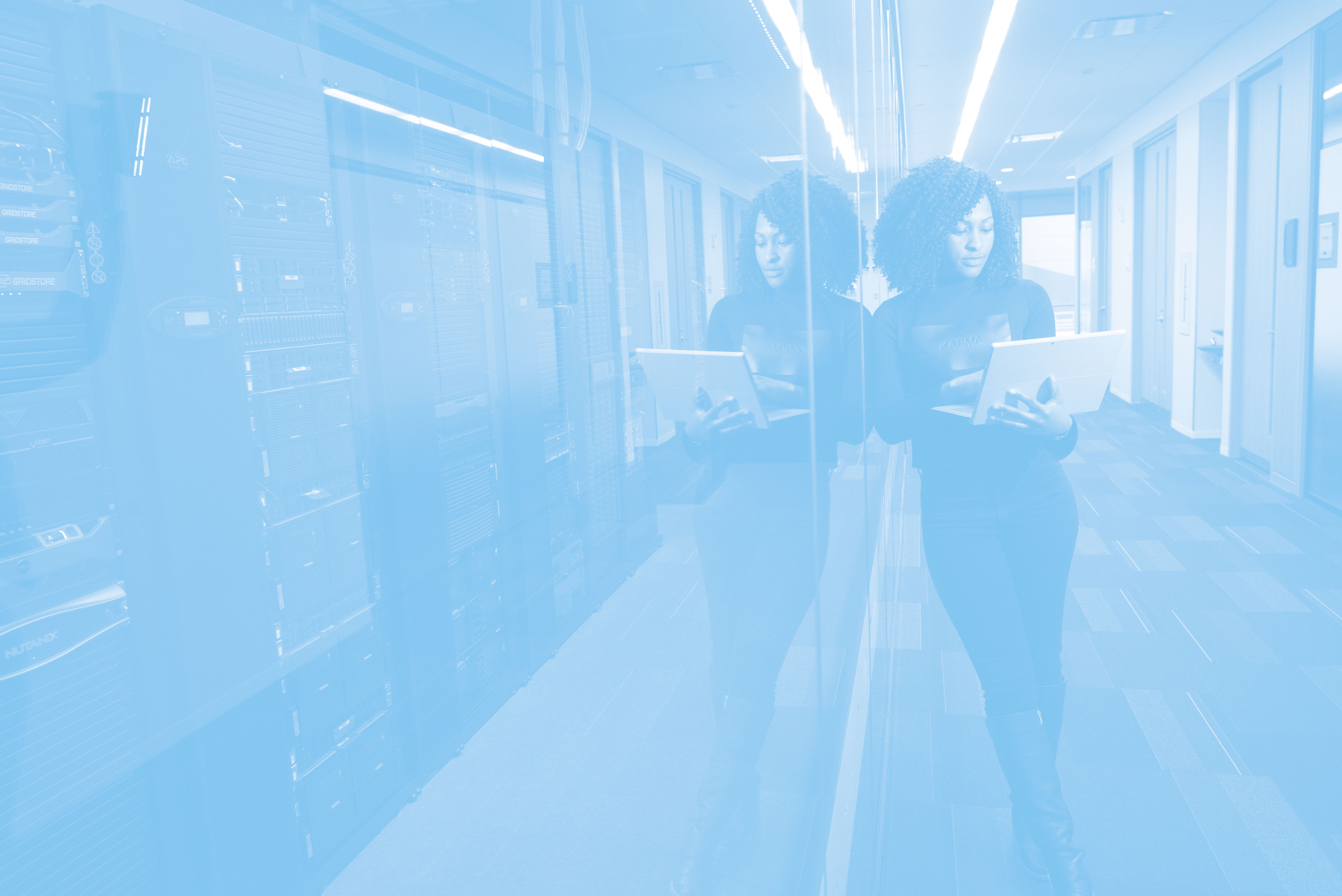 Eine IT-Spezialistin in einem Serverraum, die mit einem Laptop arbeitet, spiegelt sich in einer Glaswand – symbolisiert Technologie und Datenmanagement.